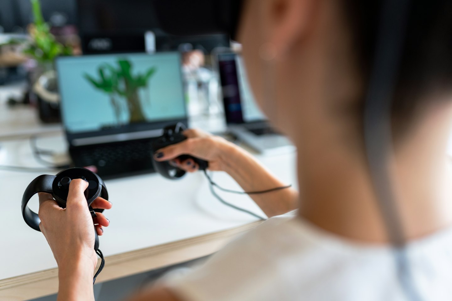 Person wearing VR headset uses controllers at a desk.