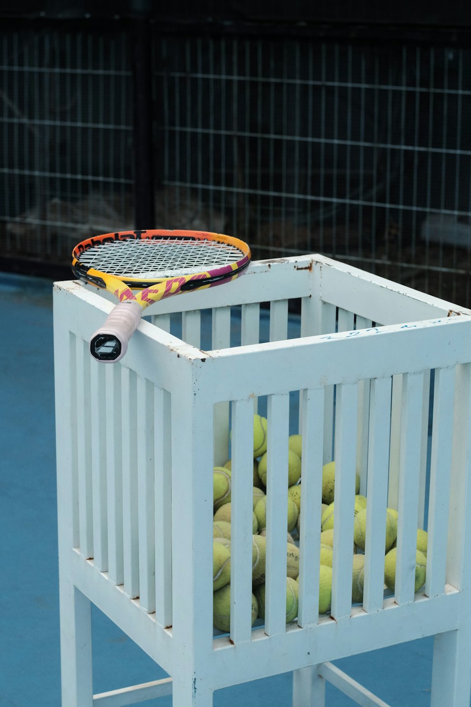 Tennis racket resting on a cart full of tennis balls.