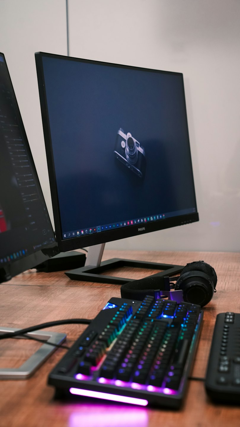 Two computer monitors and accessories on a wooden desk.